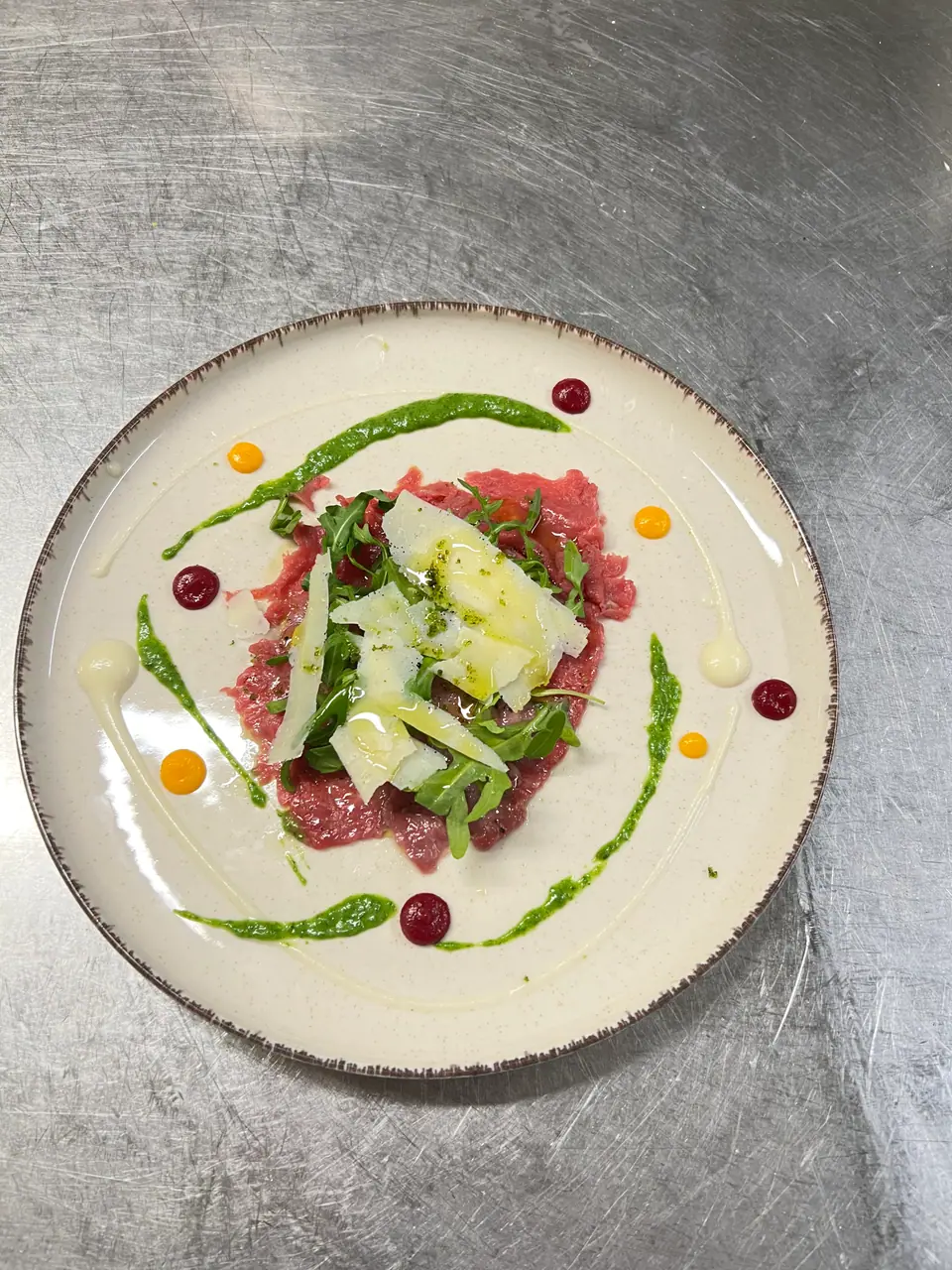 Rindercarpaccio mit Rucola und Parmesan, angerichtet auf hellem Teller